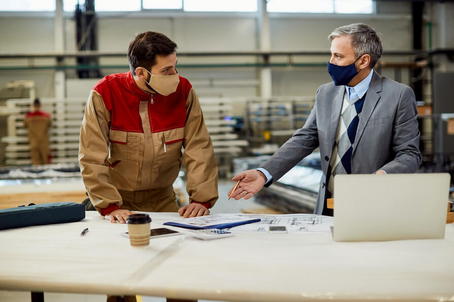 Project manager talking to carpenter while examining blueprints in a workshop